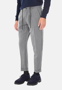Pantaloni grigi su misura con vita regolabile, davanti plissettato e gamba affusolata, abbinati a scarpe in suede blu navy e calze nere.