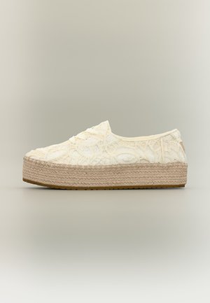 Basket blanche à plateforme en dentelle avec semelle épaisse en jute tissée et lacets blancs sur fond neutre.