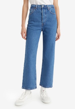 Jeans de mezclilla azul de cintura alta con corte recto, que cuentan con cinco bolsillos y detalles de costura sutiles. Combinados con zapatillas deportivas blancas.