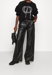 Pull noir en maille avec un détail graphique blanc, associé à un pantalon en cuir noir ample. Accessoirisé d'un petit sac à main noir et de baskets noires.