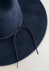 Cappello di feltro blu navy a falda larga con superficie liscia, dotato di un nastro abbinato attorno alla base. I bordi sono finemente cuciti per garantirne la durata.