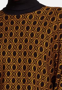 Gestrickter Pullover mit einem schwarz-gelben Muster aus abwechselnden ovalen Formen. Verfügt über einen hohen Kragen und strukturierte Stoff.