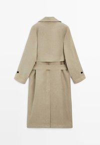 Beige lang trenchcoat med bred krave, bælte i taljen, knapmanchetter og bagstykke med detalje.
