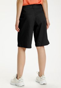 Black knee-length shorts with a smooth texture, featuring two back pockets and a clean hem. Paired with white athletic shoes.