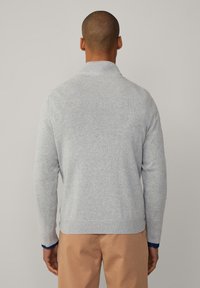 Suéter de punto gris con cuello tipo chal, puños acanalados y dobladillo. La tela tiene una textura suave y un acabado liso. Se muestra desde la parte trasera.