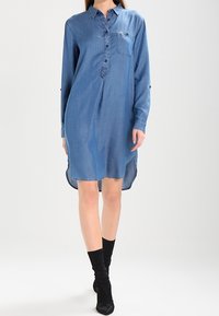 Denimklänning med krage, framknappar och bröstficka. Långa ärmar med möjligheten att rulla upp och en längre bakre fåll.