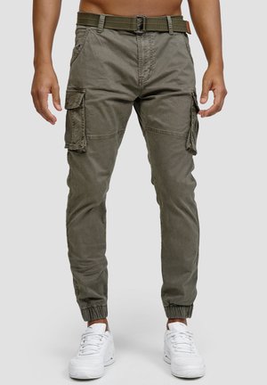 Pantalons cargo en mélange de coton vert olive, dotés de plusieurs poches latérales, d'une ceinture, de poignets élastiques et d'une coupe décontractée. Portés avec des baskets blanches.