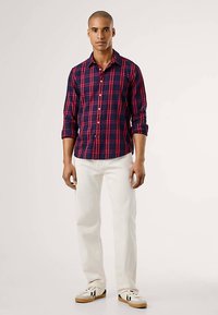 Tengerészkék és piros kockás ing, hosszú ujjakkal, felhajtva a könyöknél, fehér farmerral és fekete részletekkel ellátott tornacipővel párosítva.