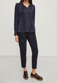 Navy silk blouse with a V-neck and tie detail, paired with navy cargo pants featuring side pockets and a textured finish. Brown slip-on shoes.