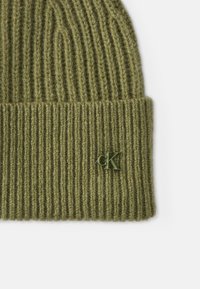Gorro verde de malha com textura canelada e bainha dobrada. Apresenta um pequeno logótipo "CK" verde de lado. Feito de material suave e quente.