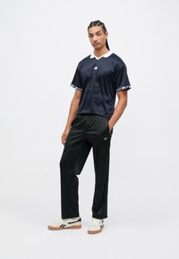 Cămașă cu imprimeu marin, cu mânecă scurtă și guler alb, asortată cu pantaloni negri și adidași crem cu accente negre.