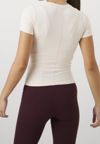 Lyhytnä sleeves -tiukka, vaaleanpunainen paita, jossa on sileä pinta ja keskivaiheessa sauma, yhdistetty tumman burgundin värisiin korkeavyötäröisiin leggings-housuihin.