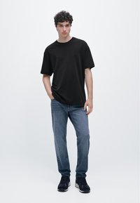 Black short-sleeve T-shirt with a relaxed fit, paired with light blue denim jeans and black sneakers. Plain design, no patterns or graphics.