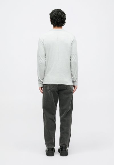 Šviesiai pilka, ilgomis rankovėmis marškinėliai su tiesia nugaros siūle, derinami su tamsiai pilkomis kelnėmis. Lygus tekstūra, laisvas siluetas ir sluoksniuotas vaizdas su avalyne.