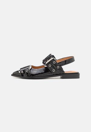 Sort sandal i laklæder med flad sål, spids tå, sølvspænde, stropper og slingback-hæl på hvid baggrund.