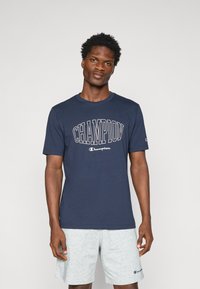 Navyblaue Baumwoll-T-Shirt mit weißem, über einem Logo gewölbtem "CHAMPION"-Text. Rundhalsausschnitt, kurze Ärmel und eine normale Passform.