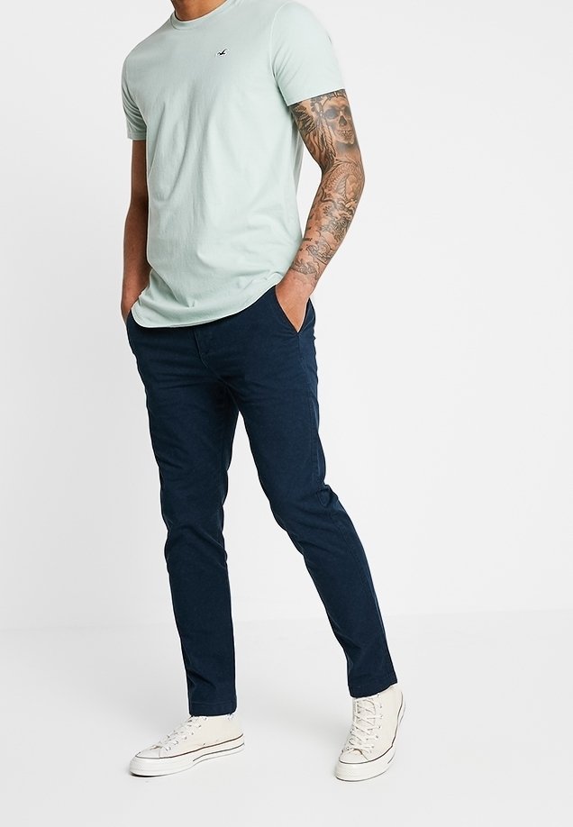 Světle modré bavlněné tričko s kulatým výstřihem a malým logem, spojené s námořnickými slim-fit chino kalhotami a bílými plátěnými teniskami.