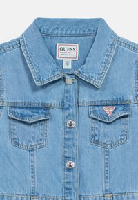 Γαλάζιο τζιν τζάκετ με γιακά, δύο τσέπες στο στήθος, ασημένιες λεπτομέρειες κουμπιών και τρίγωνο λογότυπο μάρκας στην αριστερή τσέπη.