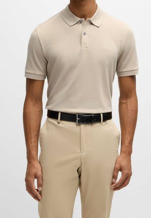 Beżowa koszulka polo z krótkim rękawem, kołnierzykiem i dwoma guzikami, zestawiona z beżowymi spodniami i czarnym skórzanym paskiem.