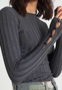 Haut gris à manches longues côtelé avec une silhouette ajustée, comportant des découpes aux poignets et un design texturé sur toute la surface.