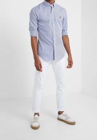 Blå- och vitrandig skjorta med krage, slim fit. Buren tillsammans med vita uppvikta byxor och vita sneakers med bruna sulor.