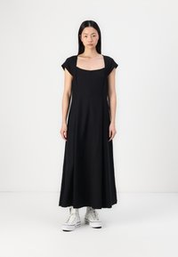 Zwarte katoenen maxi-jurk met korte kapmouwen, vierkante halslijn en een A-lijn silhouet, gecombineerd met witte hoge sneakers.
