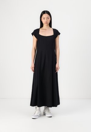 Zwarte katoenen maxi-jurk met korte kapmouwen, vierkante halslijn en een A-lijn silhouet, gecombineerd met witte hoge sneakers.