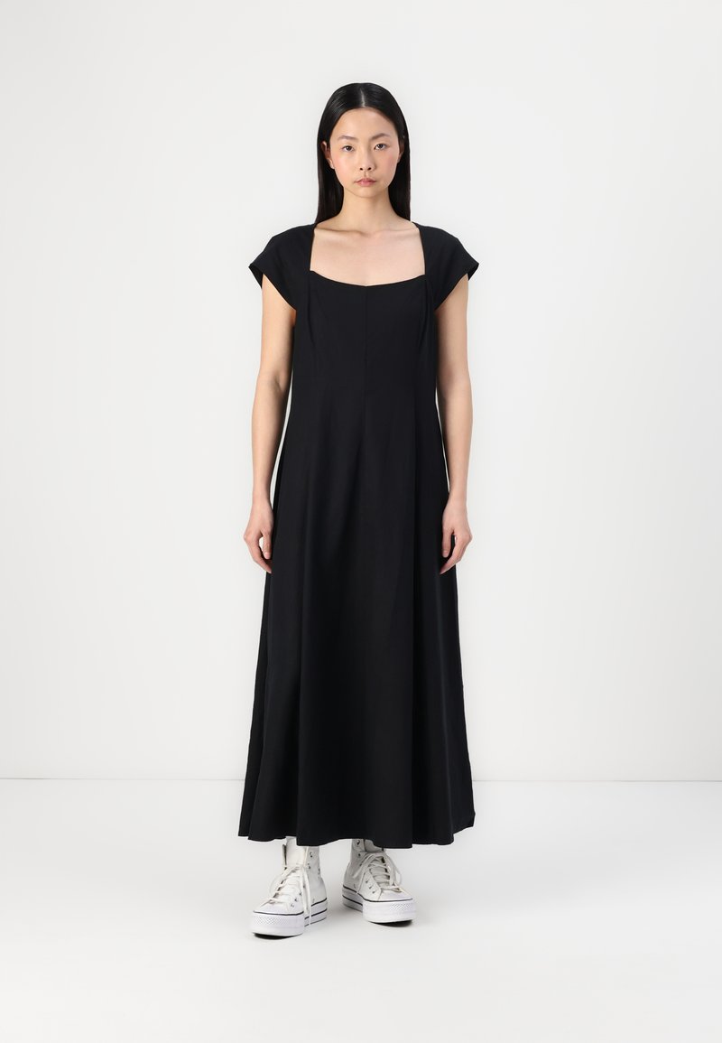 Zwarte katoenen maxi-jurk met korte kapmouwen, vierkante halslijn en een A-lijn silhouet, gecombineerd met witte hoge sneakers.