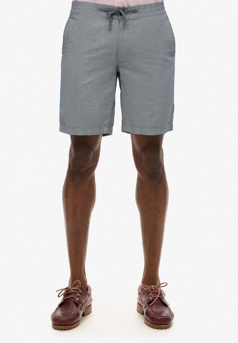 Shorts chino à rayures bleues et blanches, dotés d'une taille élastique avec cordon de serrage, de poches latérales et d'une coupe décontractée, assortis à des chaussures brunes.