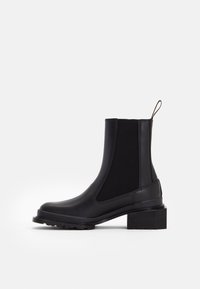 Svart ankelboot som har en slät läderkropp, elastiska sidopaneler, en dragrem baktill och en chunky, texturerad klack.