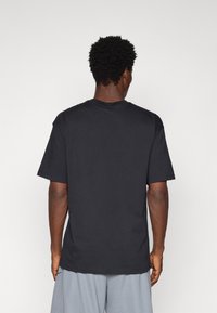 Czarny bawełniany T-shirt z krótkimi rękawami i okrągłym dekoltem, o prostym designie bez widocznych logo czy wzorów. Widok z tyłu.
