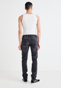 Vaqueros negros con un corte ajustado, costuras en contraste y dos bolsillos traseros. Llevados con una camiseta sin mangas blanca y zapatillas negras.