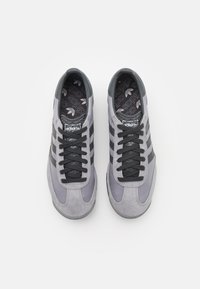 Sneakers in suede grigio con strisce nere, lacci testurizzati e una soletta con motivo e logo Adidas. Punta arrotondata e suola imbottita.