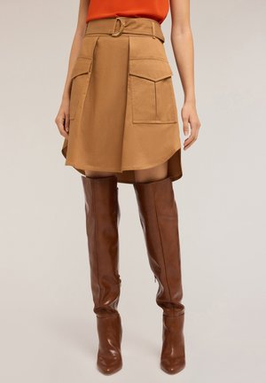 Tan A-line skirt with two large front pockets and a belt, paired with brown knee-high leather boots. Smooth texture, casual design.