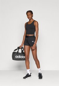 Μαύρο αθλητικό μπλουζάκι και σορτς με λογότυπο. Κρατώντας μια μαύρη τσάντα duffel της Adidas με αντίθετο λευκό λογότυπο.