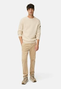 Beige ribbed sweater, beige corduroy pants, and light brown textured sneakers. The outfit features a crew neckline and relaxed fit.
