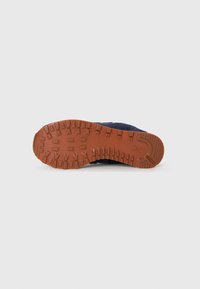 Semelle d'une sneaker bleu marine avec un profil en caoutchouc marron et un logo embossé près du talon, présenté sur un fond blanc uni.