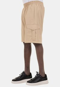 Pantaloni cargo beige con cintura elastica, tasche laterali e tasca frontale con flap. Abbinati a sneaker nere con suole bianche.