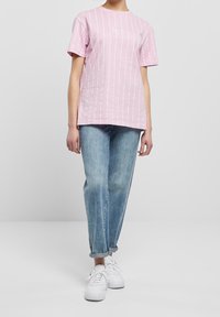 Růžové pruhované tričko s krátkým rukávem, kulatým výstřihem a bílými linkami, spárované se světlými modrými volnými džíny a bílými teniskami.