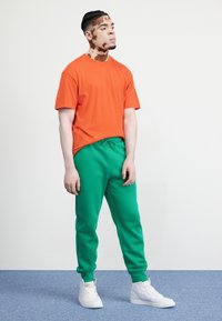 Orange bomulls t-shirt och gröna sweatpants med elastisk midja. Bärs med vita hög-top sneakers. Slät, avslappnad design utan mönster.