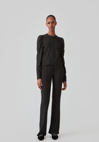 Sort stribet outfit bestående af en tætsiddende top med puffede ærmer og vide bukser, der fremhæver hvide lodrette striber og en glat tekstur.