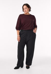 Bordový textúrovaný top s dlhým rukávom a spadnutými ramenami, skombinovaný s čiernymi vysokými nohavicami širokého strihu a čiernymi podpätkovými topánkami.