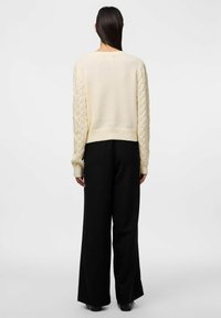 Maglione beige a lavorazione a maglia con maniche lunghe e orlo corto, abbinato a pantaloni neri a gamba larga. Texture liscia, senza motivi visibili.