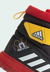 Mustikkapuna sneaker, jossa on pehmustettu punainen fleecekaulus, keltaiset yksityiskohdat ja sivussa sarjakuvamainen Mikki Hiiri -kuvio.