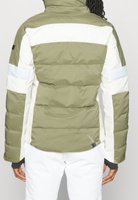 Giubbotto imbottito che presenta una combinazione di colori verde oliva e bianco. Il design include strisce orizzontali e una finitura testurizzata.