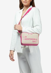 Borsa a spalla in tela color beige con accenti rosa brillante; presenta una forma rettangolare e testo stampato: "IO SONO UNA BORSA RESPONSABILE."