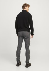Schwarzer Strickrollkragenpullover und graue gemusterte schmal zulaufende Hose. Die Hose hat ein dezentes Hahnentrittmuster. Das Model wird von hinten gezeigt.
