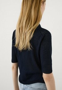 Mørkeblå kortærmet striktop med et struktureret, åbent vævdesign, der har en rund halsudskæring og en afslappet pasform, parret med lyse denim jeans.