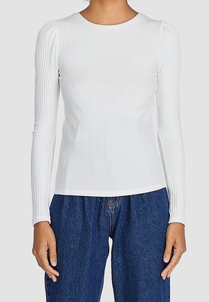 Haut à manches longues rayé blanc avec un col rond, présentant des épaules bouffantes et une silhouette ajustée, associé à un jean bleu taille haute.