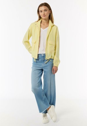 Yellow zip-up jacket with two front pockets and drawstring hem. Paired with light blue wide-leg jeans and white sneakers.